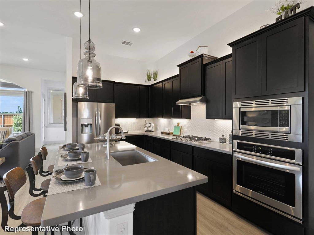 2204 Ridgecrest Lane Anna, TX 75409 - Photo 3 of 17 Modern kitchen featuring dark cabinetry, stainless steel appliances, a center island with sink, and pendant lighting
