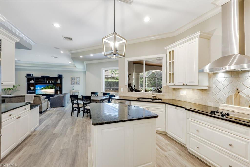 3960 Deep Passage Way Naples, FL 34109 - Photo 14 of 34 Kitchen featuring pendant lighting, wall chimney range hood, tasteful backsplash, ornamental molding, and dark stone countertops