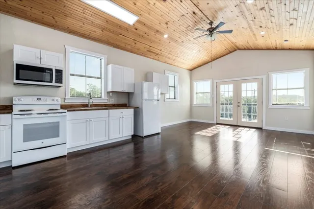 a kitchen with stainless steel appliances a stove top oven a sink dishwasher a refrigerator and white cabinets with wooden floor