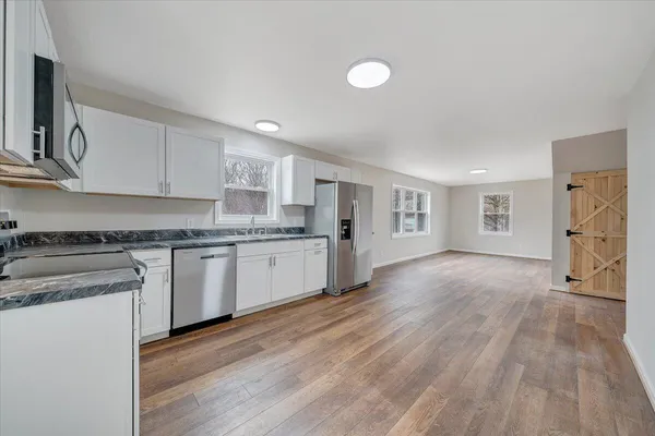 a kitchen with granite countertop a stove top oven a sink dishwasher and white cabinets with wooden floor