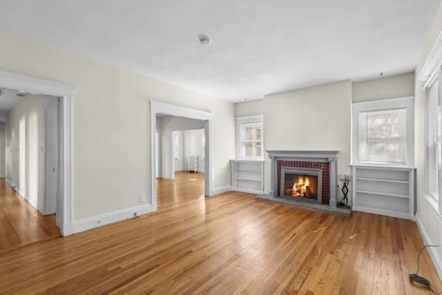 a view of an empty room with wooden floor fireplace and a window