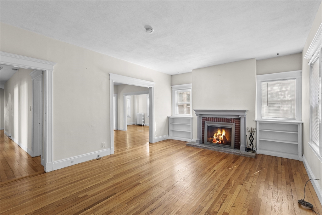 a view of an empty room with wooden floor fireplace and a window