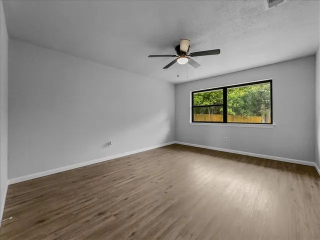 a view of a room with wooden floor ceiling fan and windows