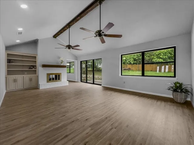 an empty room with wooden floor fireplace and windows