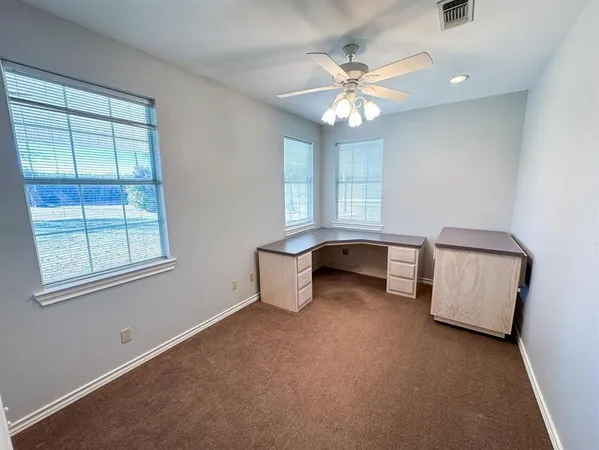 an empty room with chandelier fan and windows