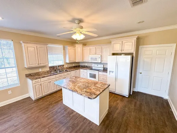 a kitchen with granite countertop a refrigerator a stove a sink and white cabinets with wooden floor