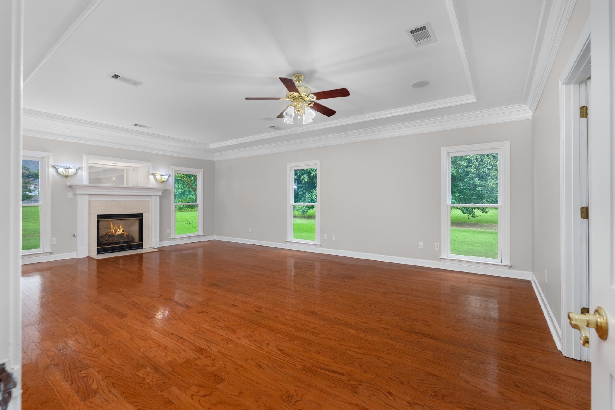 4839 Mayfield Road West Collierville, TN 38017 - Photo 34 of 40 Unfurnished living room with wood finished floors, crown molding, a raised ceiling, a premium fireplace, and ceiling fan