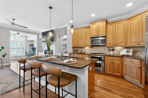 a kitchen with stainless steel appliances granite countertop wooden cabinets a stove a sink a dining table and chairs