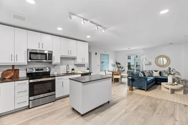 a kitchen with stainless steel appliances granite countertop a stove top oven a sink dishwasher and white cabinets with wooden floor