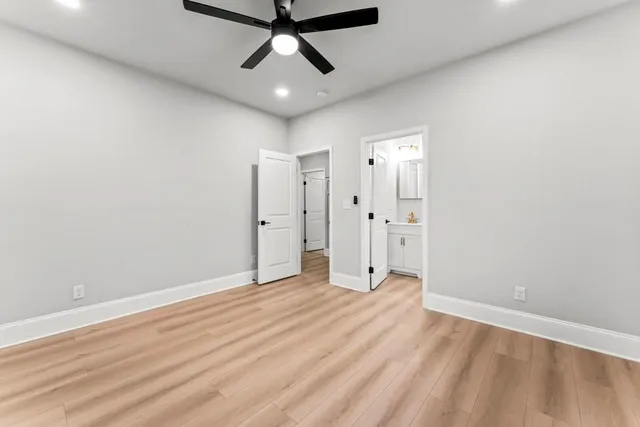 an empty room with wooden floor ceiling fan and windows