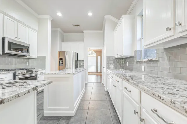 a large kitchen with stainless steel appliances granite countertop a stove a sink and white cabinets