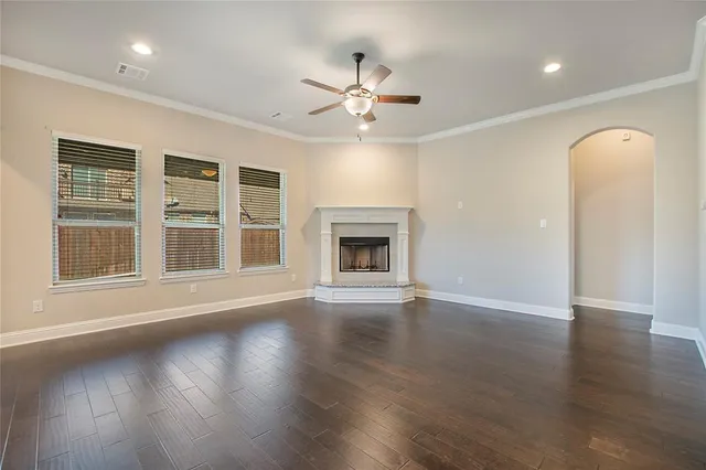 an empty room with wooden floor fireplace and a kitchen view