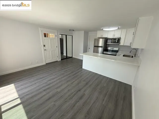 a living room with stainless steel appliances a wooden floor a large window and a fireplace