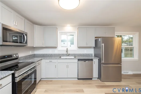 a kitchen with stainless steel appliances granite countertop a stove top oven a refrigerator a sink and dishwasher with wooden floor