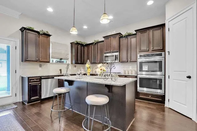 a kitchen with kitchen island granite countertop a sink cabinets and stainless steel appliances