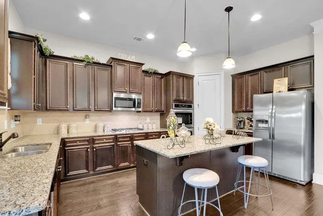 a kitchen with stainless steel appliances granite countertop a sink a stove a refrigerator cabinets and chairs