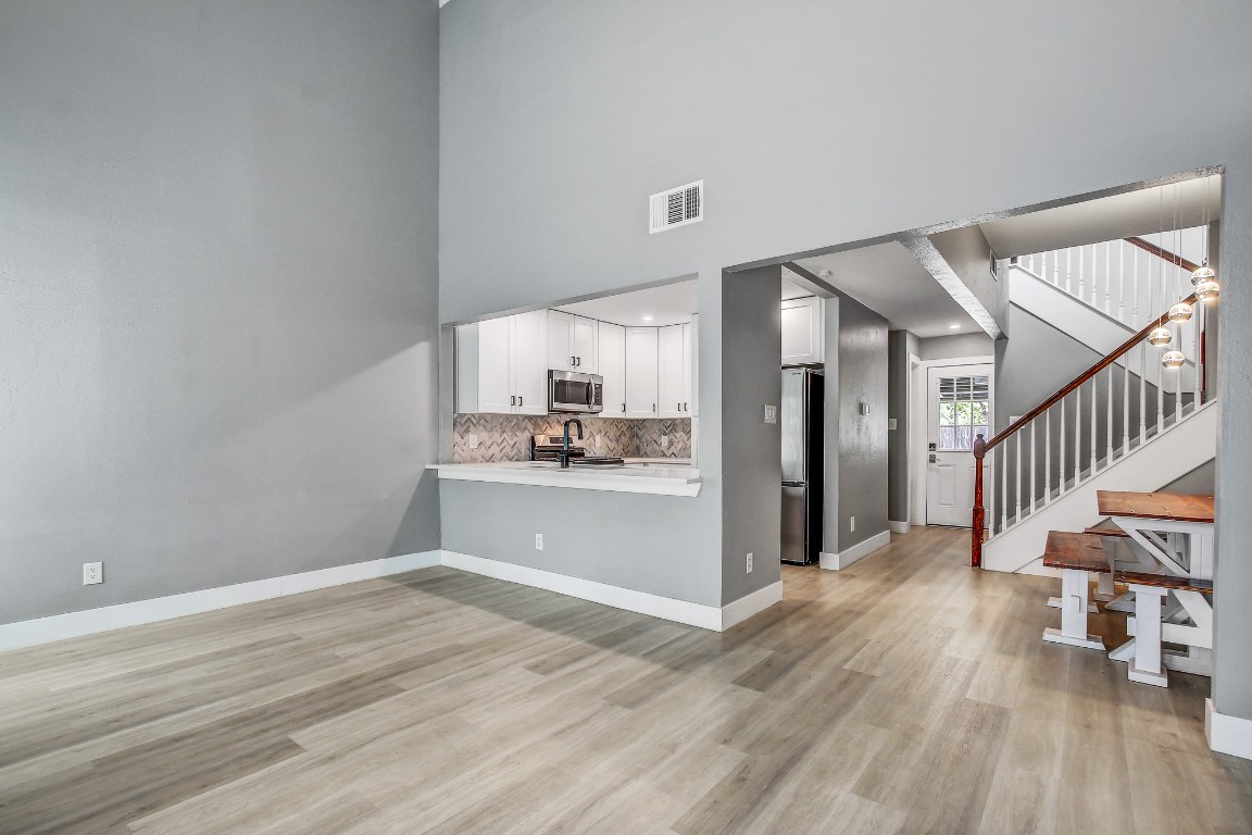1010 West Rundberg Lane, Unit 24 Austin, TX 78758 - Photo 1 of 24 Unfurnished living room with a high ceiling, light wood-style flooring, stairs, and baseboards