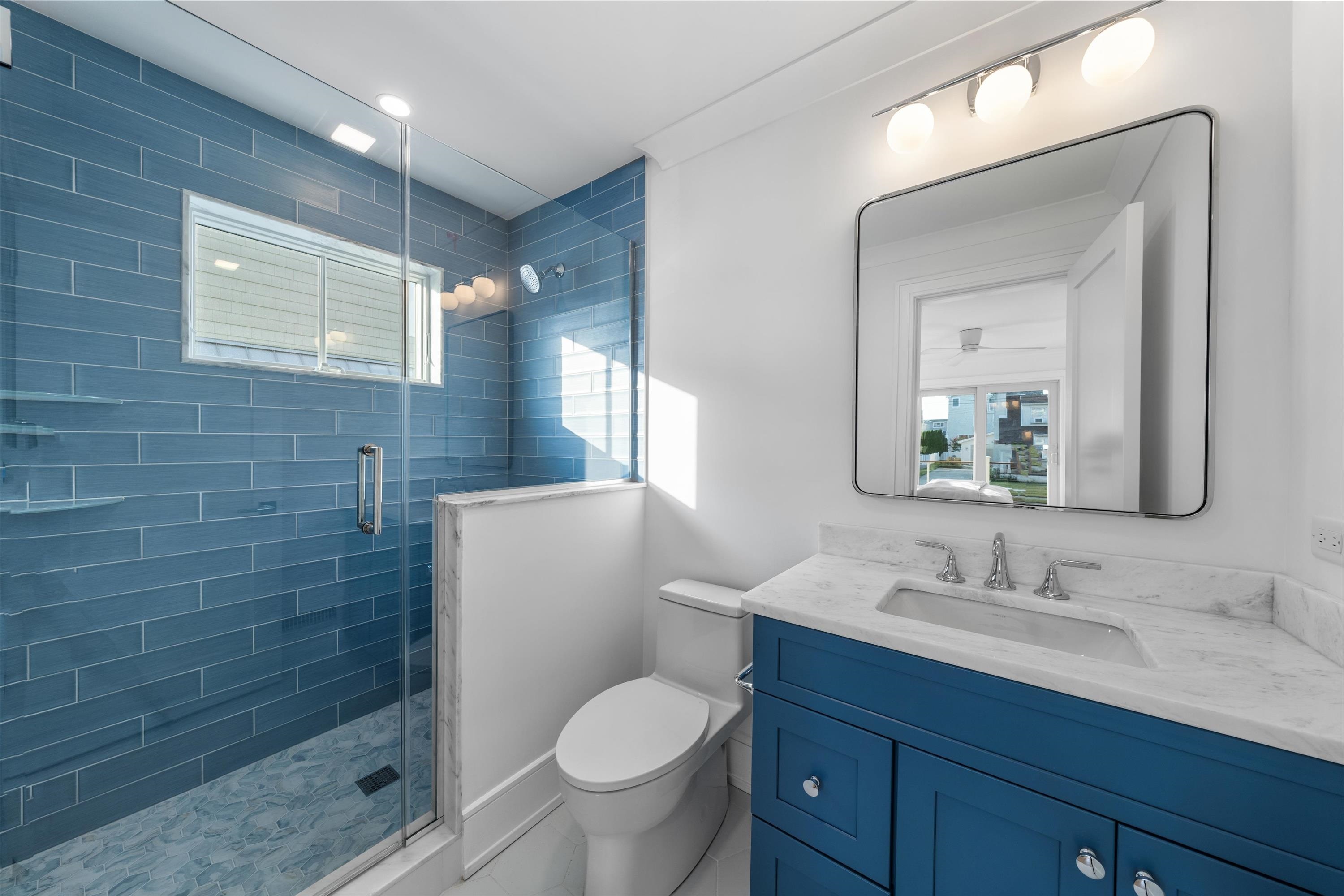 245 57th Street Avalon, NJ 08202 - Photo 30 of 50 a bathroom with a granite countertop toilet a sink a mirror and shower
