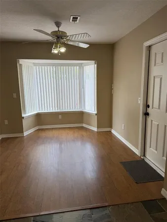 an empty room with wooden floor ceiling fan and windows