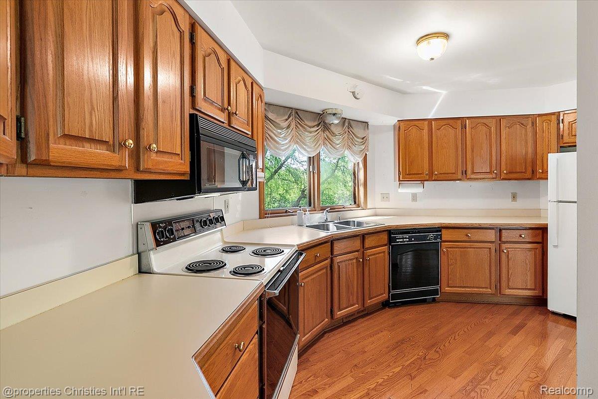 6175 Tripp Road Holly, MI 48442 - Photo 10 of 63 Kitchen featuring wood cabinetry, light-toned countertops, hardwood flooring, a stainless steel double basin sink, and a built-in microwave