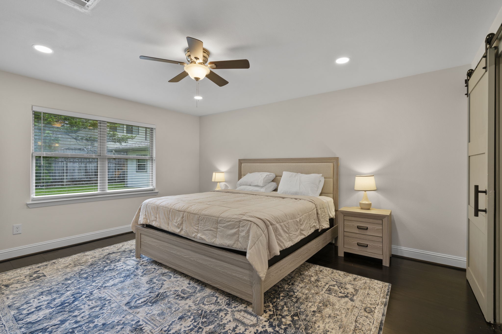 2402 Chimney Rock Road Houston, TX 77057 - Photo 14 of 36 Generous primary bedroom with ample natural light, neutral color palette, and updated flooring. Features a ceiling fan and sliding barn-style closet door.
