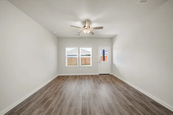 an empty room with wooden floor ceiling fan and windows