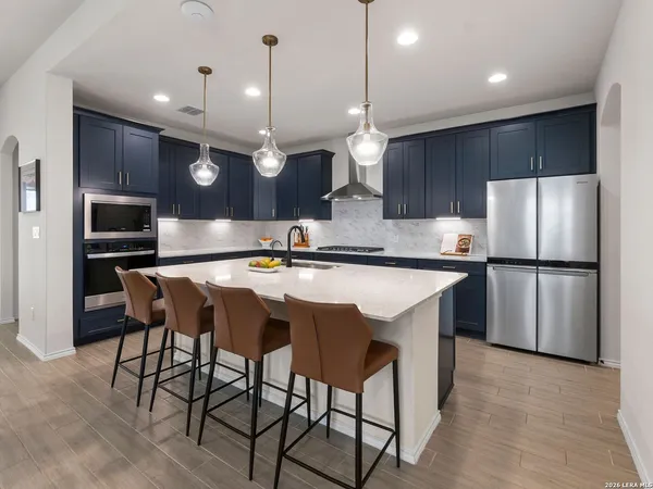 a kitchen with stainless steel appliances granite countertop a sink a stove a refrigerator and island with wooden floor
