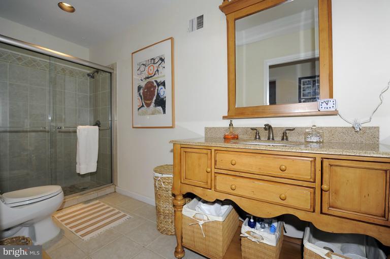 7720 Greentree Road Bethesda, MD 20817 - Photo 9 of 23 a bathroom with a granite countertop sink a mirror a toilet and a shower