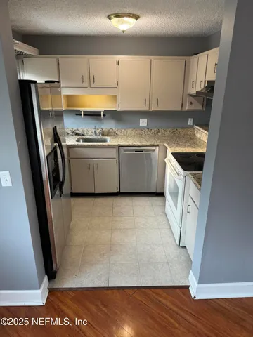 a kitchen with granite countertop a refrigerator a sink a stove and white cabinets