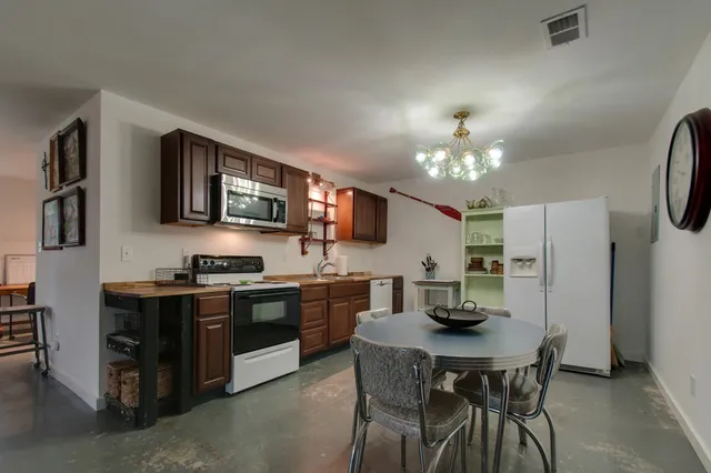 a kitchen with stainless steel appliances granite countertop a stove top oven a refrigerator a sink dishwasher a dining table and chairs with wooden floor