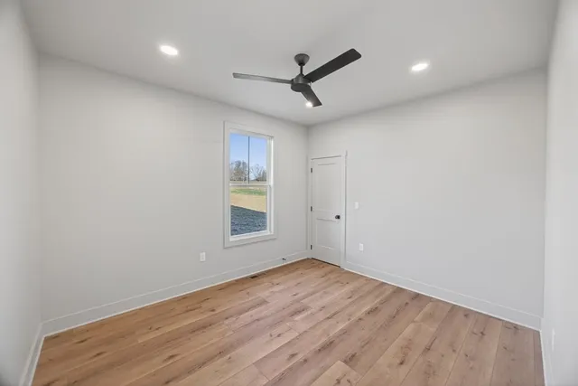 an empty room with wooden floor ceiling fan and windows