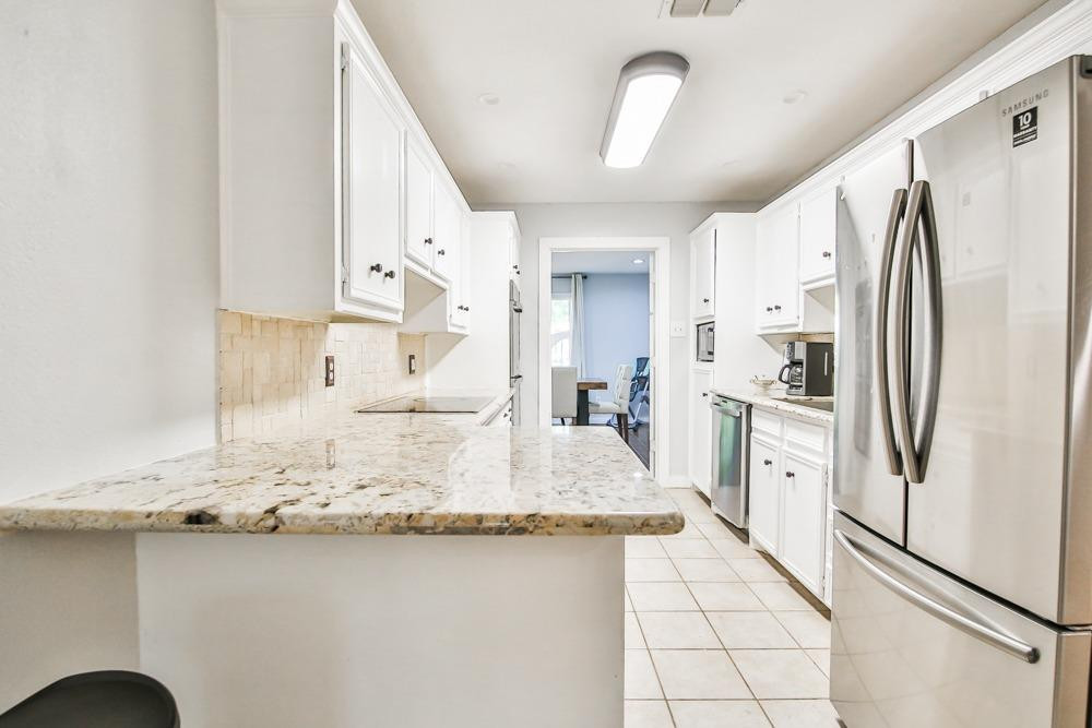 4915 79th Street Lubbock, TX 79424 - Photo 9 of 37 a large kitchen with granite countertop a refrigerator a sink and white cabinets