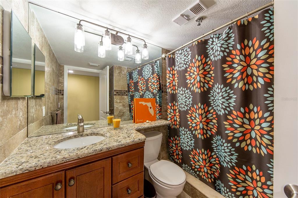 15400 Gulf Boulevard, Unit 505 Madeira Beach, FL 33708 - Photo 21 of 27 a bathroom with a granite countertop sink a toilet and shower curtain