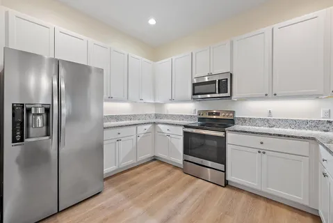 a kitchen with granite countertop a refrigerator stove and white cabinets