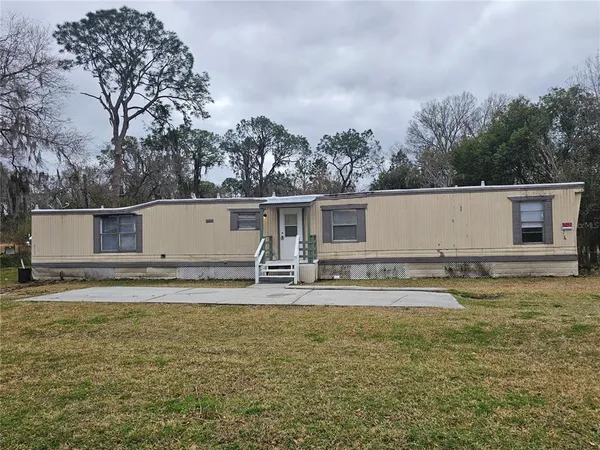 a view of a house with backyard and trees in the background