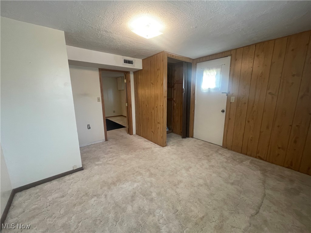 3707 River Road Vienna, WV 26105 - Photo 26 of 35 Empty room featuring light carpet, a textured ceiling, and wooden walls