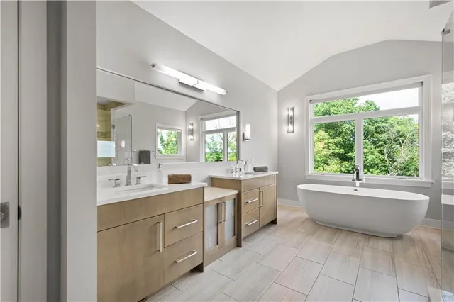 a bathroom with a granite countertop sink mirror bathtub and next to a window