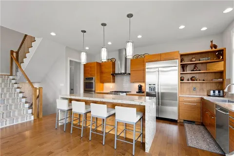 a kitchen with stainless steel appliances kitchen island granite countertop a refrigerator a stove and a wooden floors