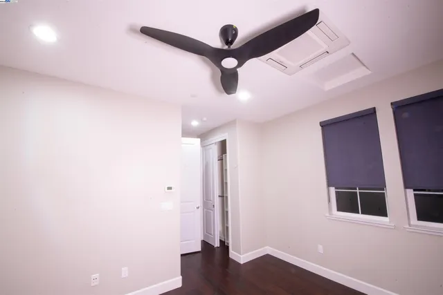 a view of an empty room with wooden floor and a ceiling fan