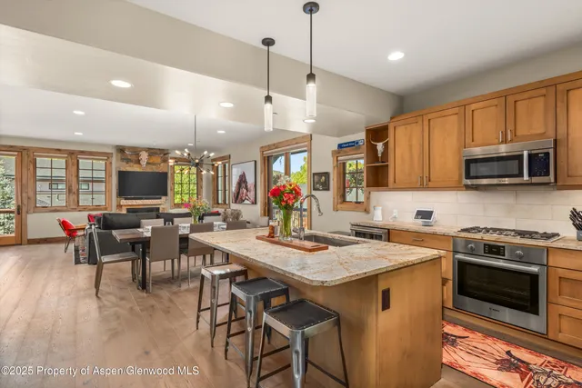 a kitchen with stainless steel appliances granite countertop a stove top oven a sink a dining table and chairs with wooden floor