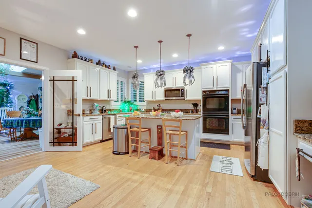 a kitchen with stainless steel appliances kitchen island granite countertop a refrigerator oven a sink a stove and white cabinets with wooden floor