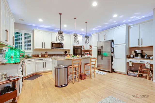 a kitchen with stainless steel appliances kitchen island granite countertop a refrigerator a stove top oven a sink dishwasher and white cabinets with wooden floor