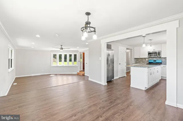 a view of an empty room with kitchen and window