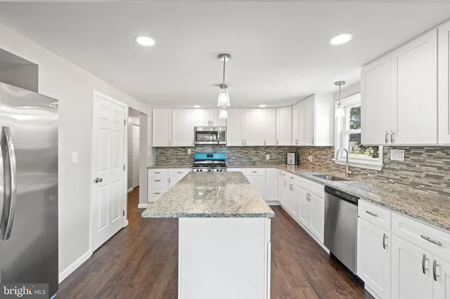 a large kitchen with stainless steel appliances kitchen island granite countertop a refrigerator and a sink