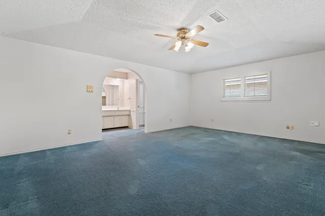 an empty room with a chandelier fan and windows