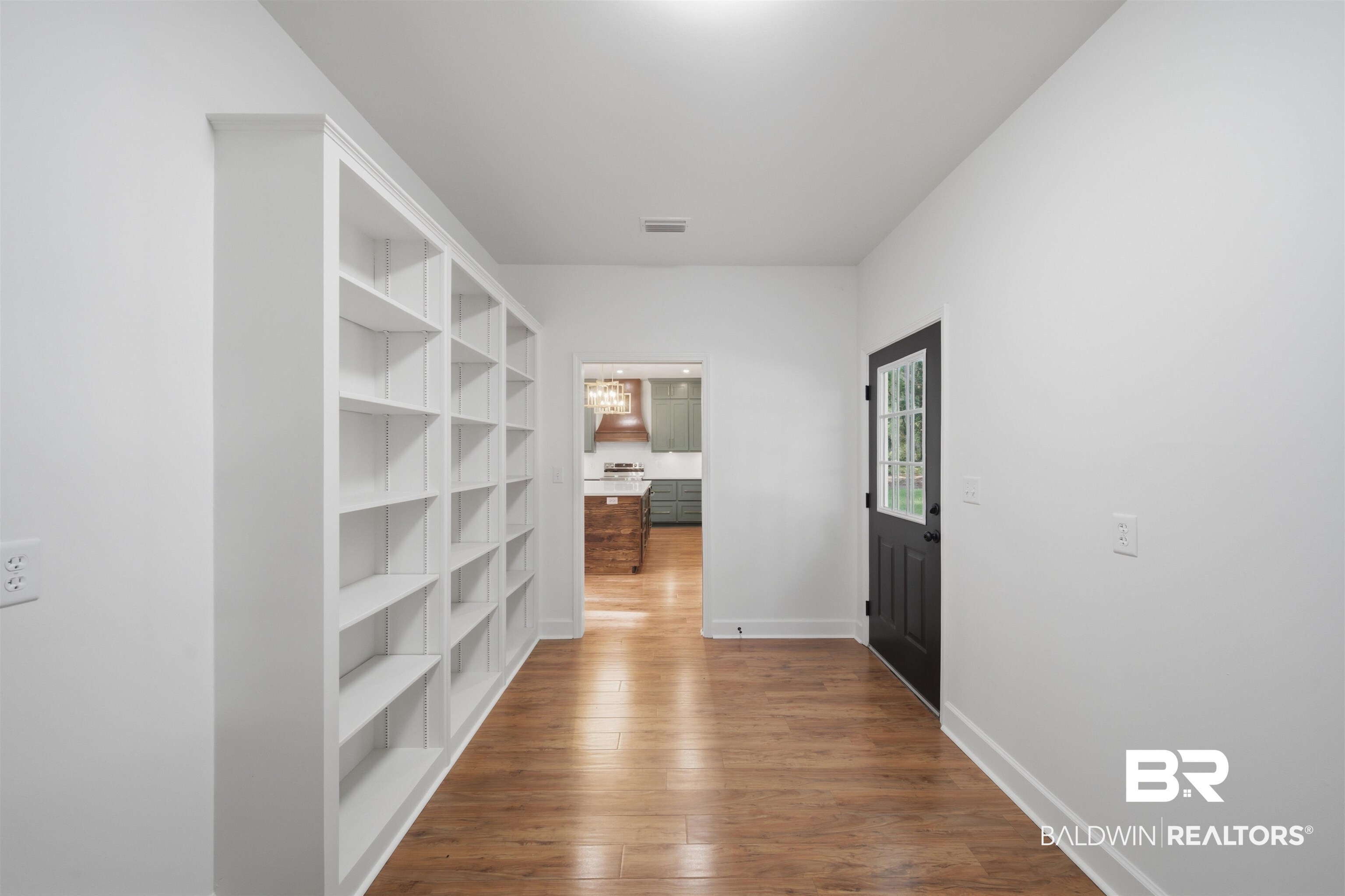 14128 Jackson Lane Foley, AL 36535 - Photo 13 of 36 Hallway featuring extensive built-in shelving, wood-finish flooring, a dark paneled door with glass inserts, and white walls