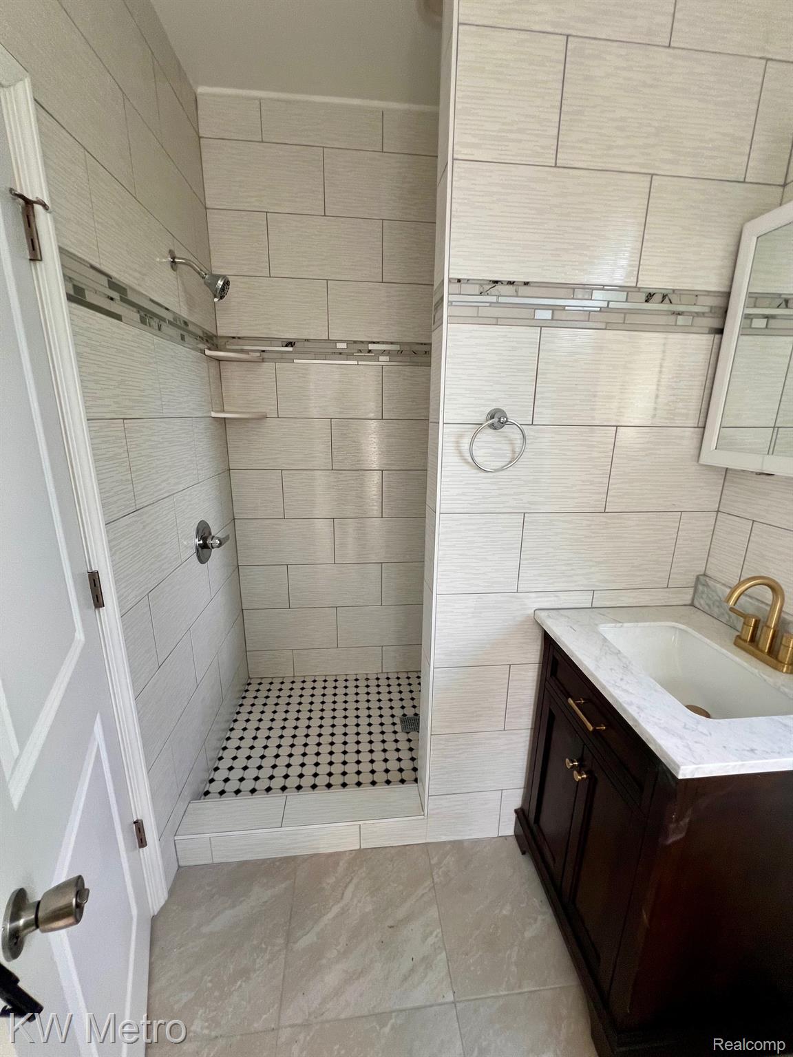939 Webb Street Detroit, MI 48202 - Photo 12 of 19 Tiled bathroom featuring a walk-in shower with mosaic floor, a dark wood vanity with white countertop, and a mirrored wall cabinet