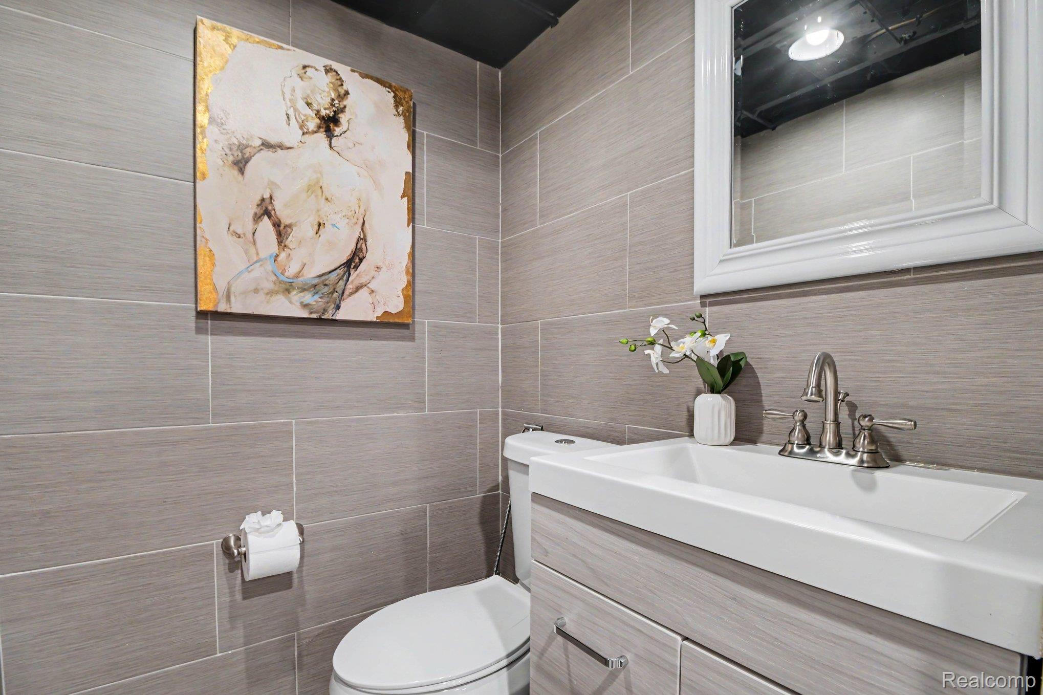 2373 Rutherford Road Bloomfield Hills, MI 48302 - Photo 21 of 28 Full-height wall tiling, single vanity with integrated sink, brushed nickel faucet, mirror with white frame, and toilet