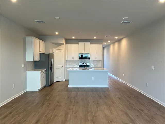 a large kitchen with stainless steel appliances kitchen island granite countertop a stove a refrigerator a sink a microwave and white cabinets with wooden floor