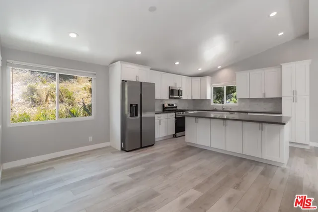 a kitchen with stainless steel appliances granite countertop a refrigerator a sink dishwasher a stove and white countertops with wooden floor